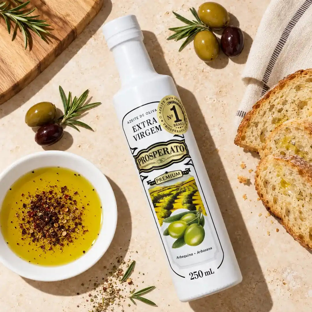Garrafa de Azeite de Oliva Extra Virgem Prosperato Premium 250 mL deitada sobre bancada clara, com tigelinha de azeite temperado com especiarias, fatias de pão, azeitonas e ramos de alecrim ao redor.