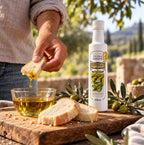 Mão molhando um pedaço de pão numa tigela de azeite ao lado da garrafa de Azeite Extra Virgem Prosperato Premium 250 mL, sobre tábua de madeira com azeitonas e paisagem de oliveiras ao fundo.