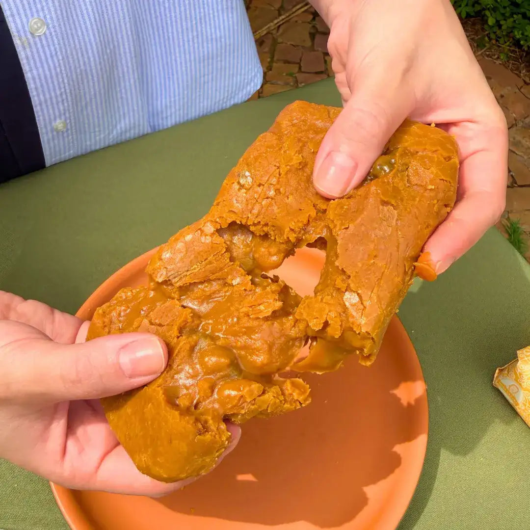 Mãos puxando bala de doce de leite com ameixa artesanal, mostrando a textura macia e elástica do puxa-puxa da Fazenda Jotacê, servida sobre prato de cerâmica laranja