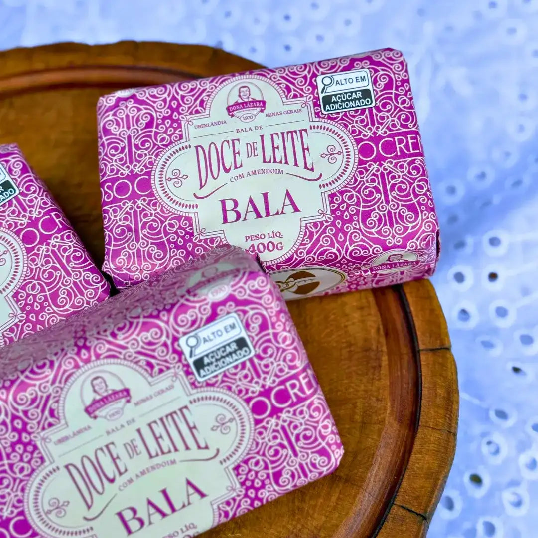 Duas embalagens rosa da bala puxa-puxa de amendoim Dona Lázara sobre tábua de madeira com toalha de renda branca ao fundo, mostrando rótulo com peso líquido 400g