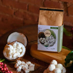 Pacote de café Bala de Coco da Fazenda Jotacê ambientado com pedaços de coco e balas de coco, sobre mesa rústica com fundo de tijolos.