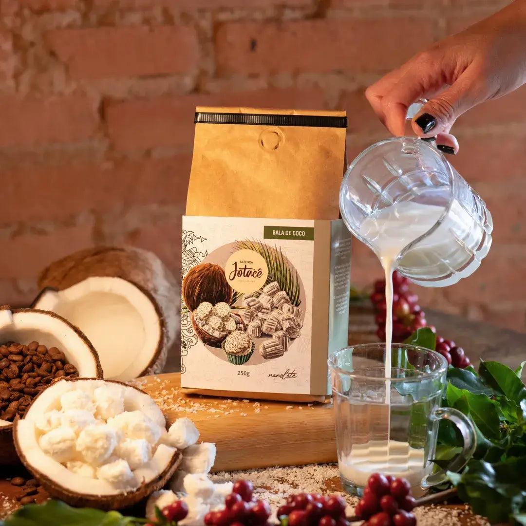 Pacote de café Bala de Coco da Fazenda Jotacê com leite sendo derramado em copo, ilustrando momento de preparo com ingredientes naturais