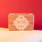 Embalagem da bala de doce de leite puxa-puxa Dona Lázara sobre fundo neutro em tons de vermelho e bege, destacando o design artesanal do produto mineiro.