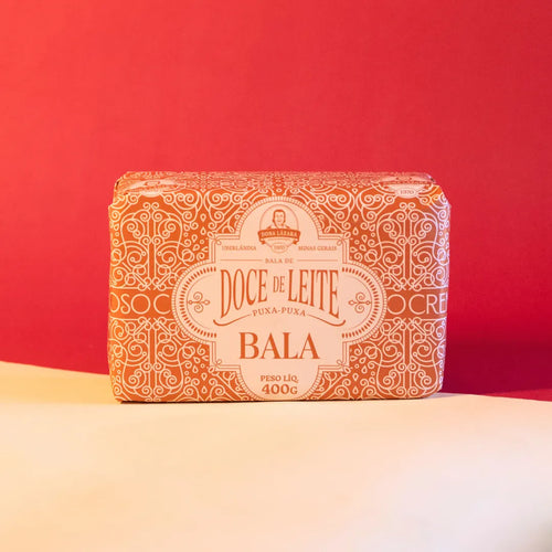 Embalagem da bala de doce de leite puxa-puxa Dona Lázara sobre fundo neutro em tons de vermelho e bege, destacando o design artesanal do produto mineiro.
