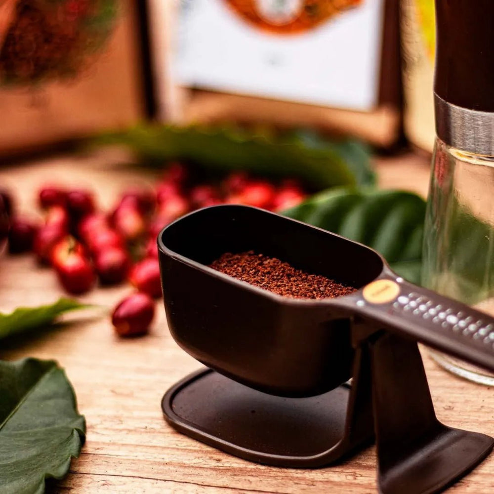 Balança dosadora dose certa da pressca acionada cheia de café em pó ao lado de pacotes e grãos de café da Fazenda Jotacê