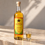 Cachaça ouro ao lado de um copinho servido, sobre bancada de pedra ao sol