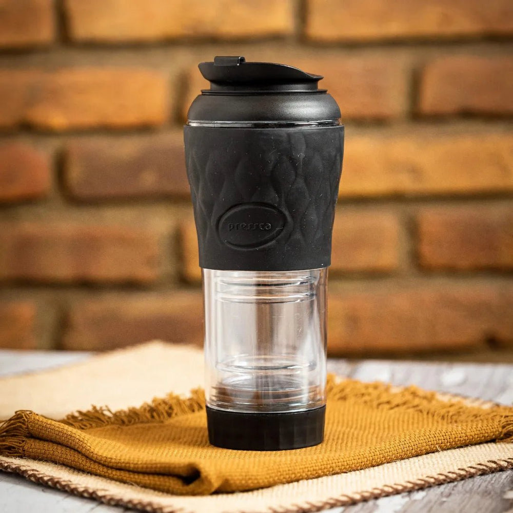 Cafeteira Portátil Pressca preta sobre um pano amarelo e fundo de parede de tijolos