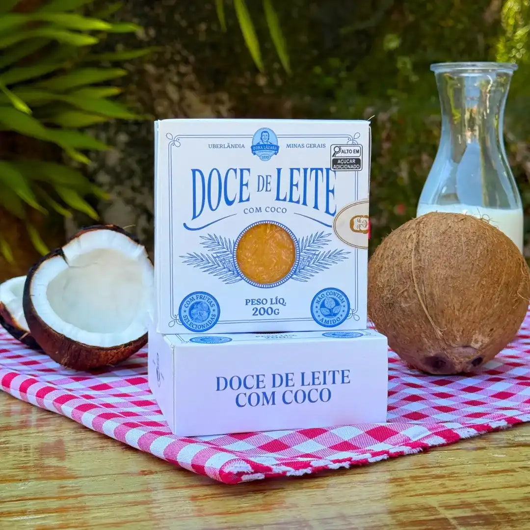 Duas caixas de Doce de Leite com Coco Dona Lázara com coco fresco e leite ao redor, sobre toalha xadrez, em composição que destaca o visual artesanal e o sabor caseiro.