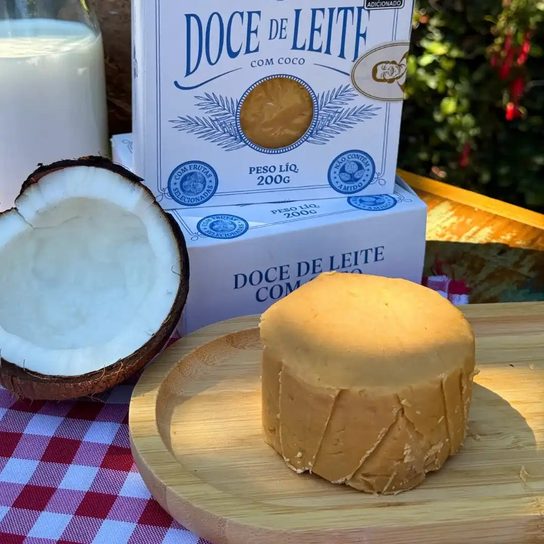 Doce de Leite com Coco Dona Lázara sobre prato de madeira, com coco partido e garrafa de leite ao fundo, mostrando a textura cremosa e artesanal do doce.