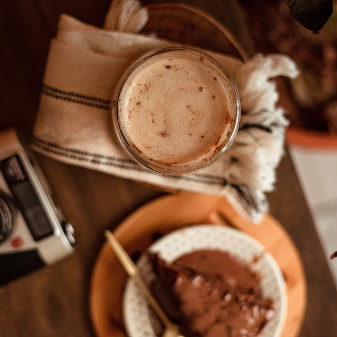 vista superior de xícara de Cappuccino Kawá da Fazenda Jotacê ao lado de um bolo de chocolate desfocado em mesa de madeira  
