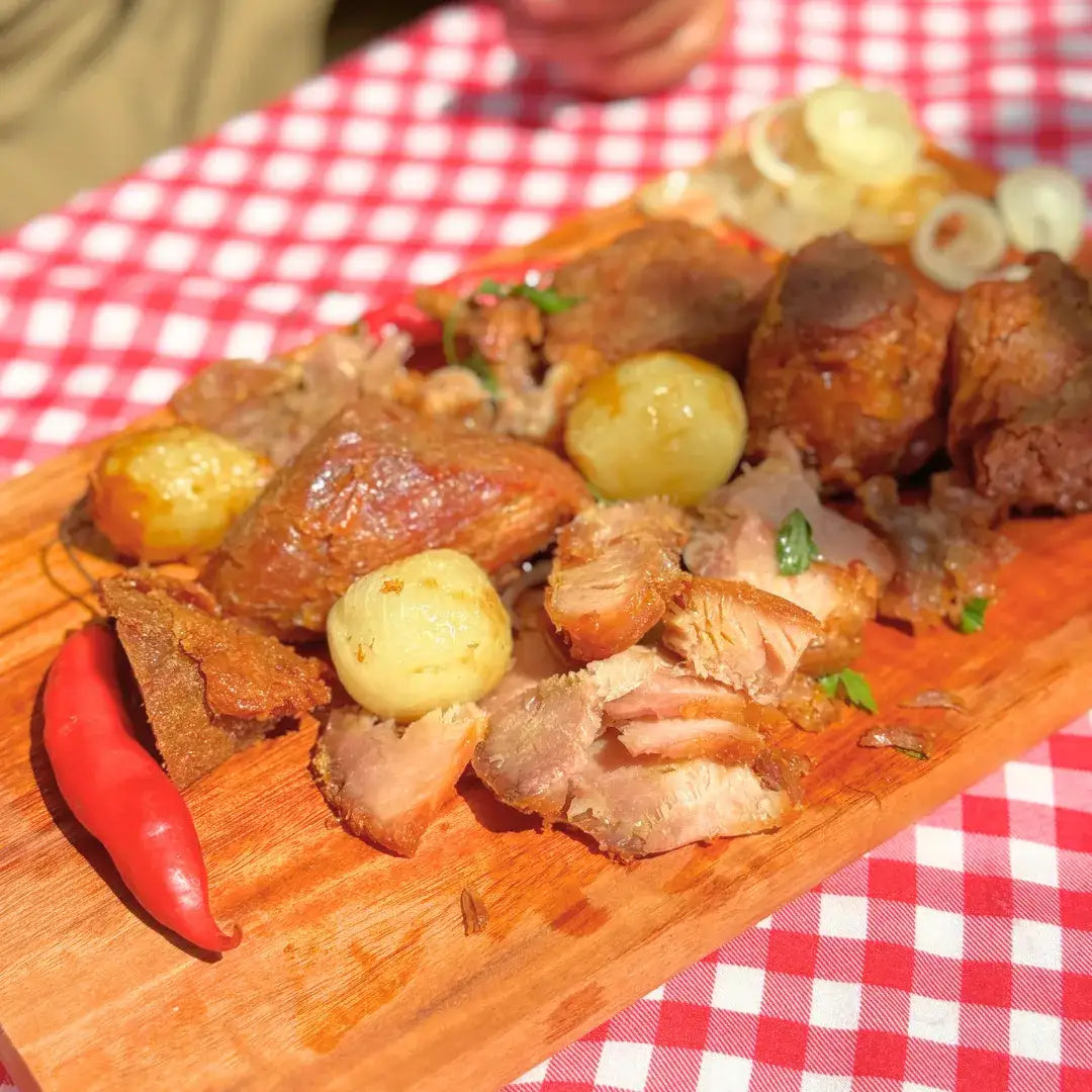 Pernil desfiado da carne na lata Xavante sobre tábua de madeira, acompanhado de batatas bolinhas, anéis de cebola e pimenta vermelha.