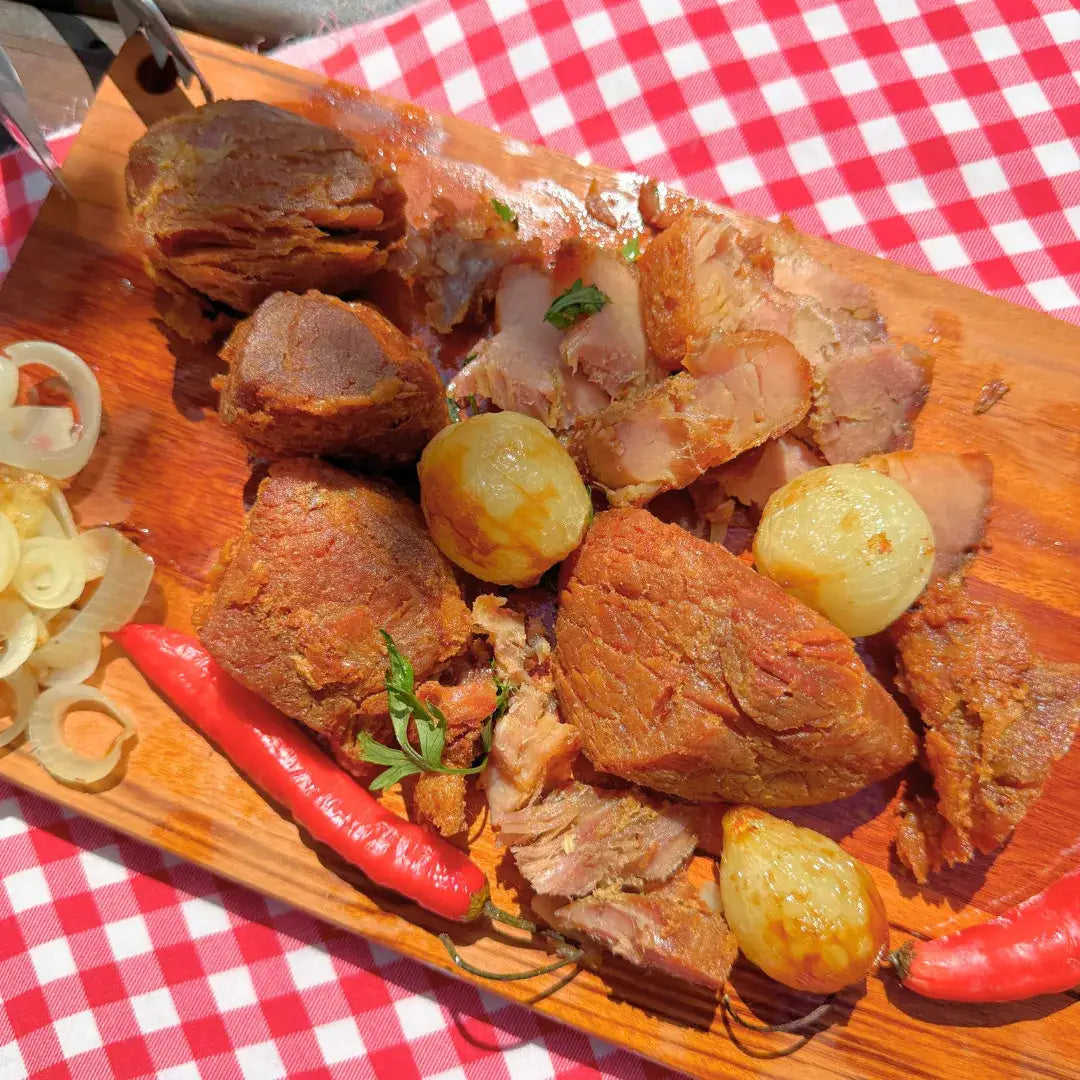Pedaços de pernil suíno confitado, retirados da lata de carne Xavante, com batatas e cebolas em tábua rústica de madeira.