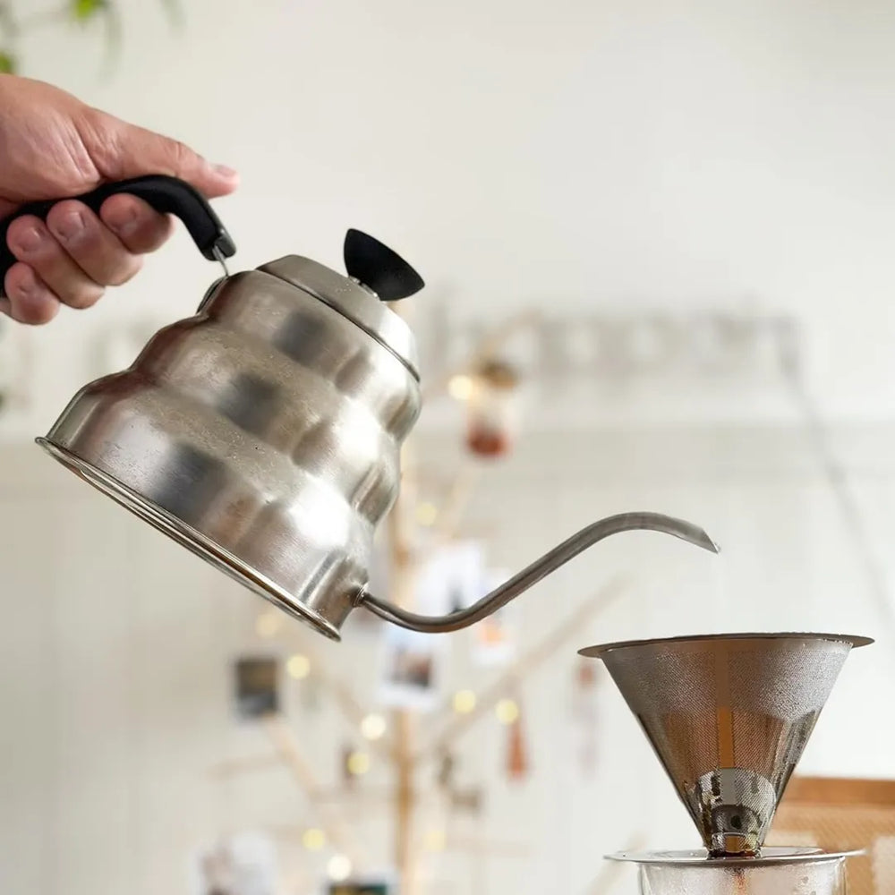 chaleira bico de ganso com alça preta da mimo style despejando agua quente em um filtro de inox para extrair café