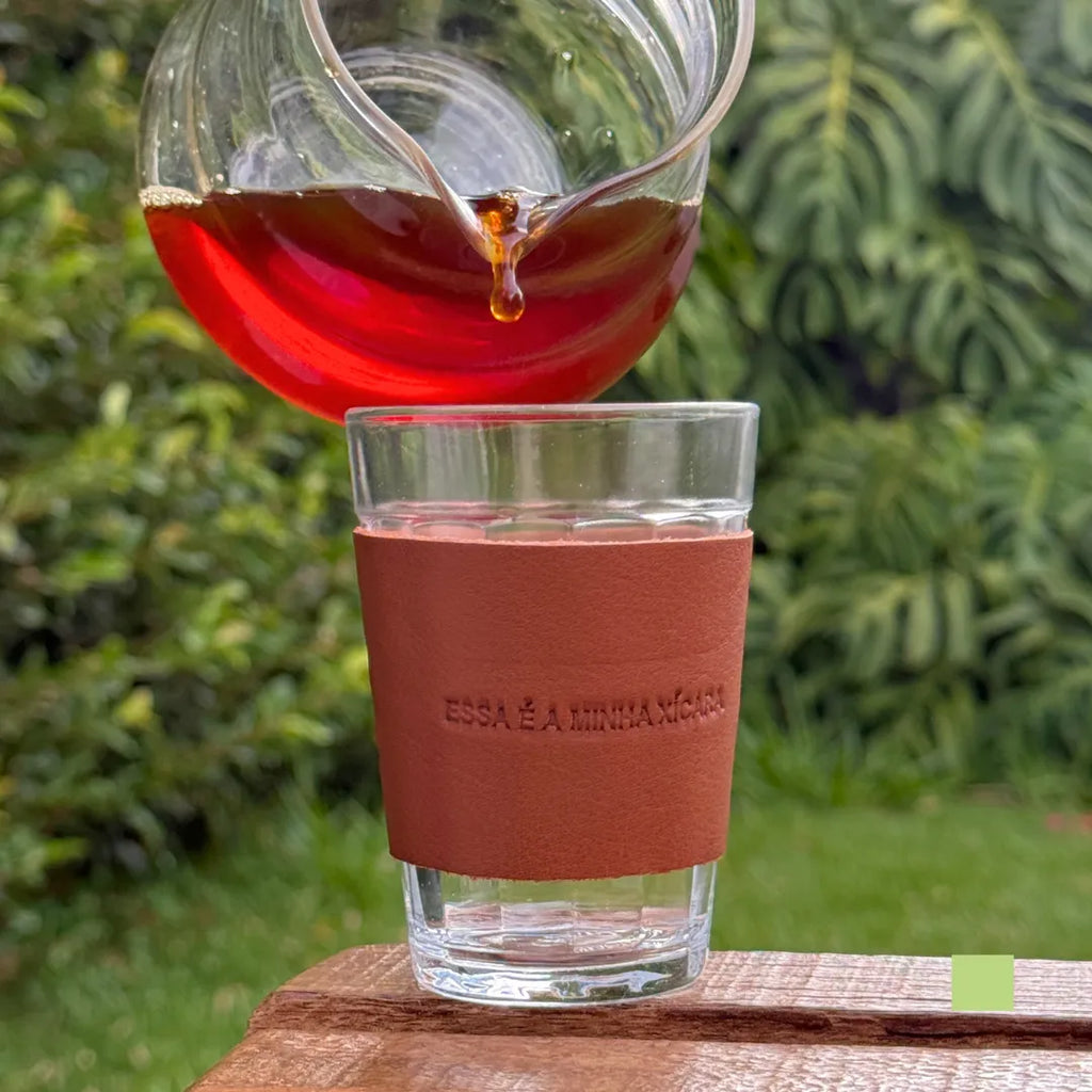 Copo americano com cinta de couro sendo preenchido com café fresco, com a frase gravada “Essa é a minha xícara” visível no couro.