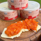 Doce de abóbora com coco artesanal servido sobre fatia de queijo minas em tábua de madeira, com três latas Dona Lázara 400g empilhadas ao fundo, combinação típica mineira