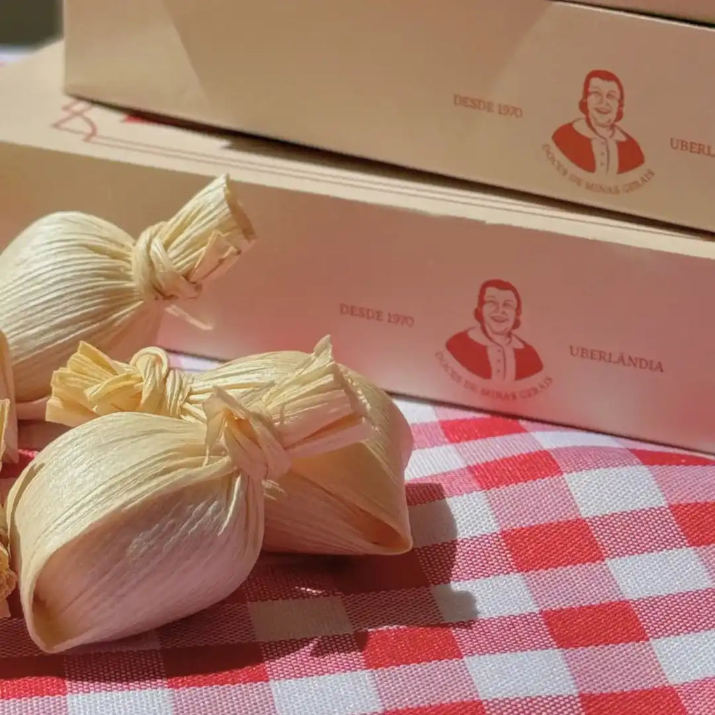 Unidades de Doce de Leite na Palha Dona Lázara sobre toalha xadrez, com caixas do produto ao fundo destacando o logotipo e o acabamento premium.