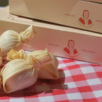 Unidades de Doce de Leite na Palha Dona Lázara sobre toalha xadrez, com caixas do produto ao fundo destacando o logotipo e o acabamento premium.