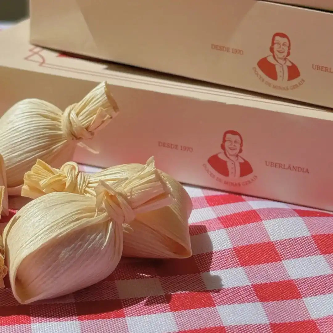 Unidades de Doce de Leite na Palha Dona Lázara sobre toalha xadrez, com caixas do produto ao fundo destacando o logotipo e o acabamento premium.