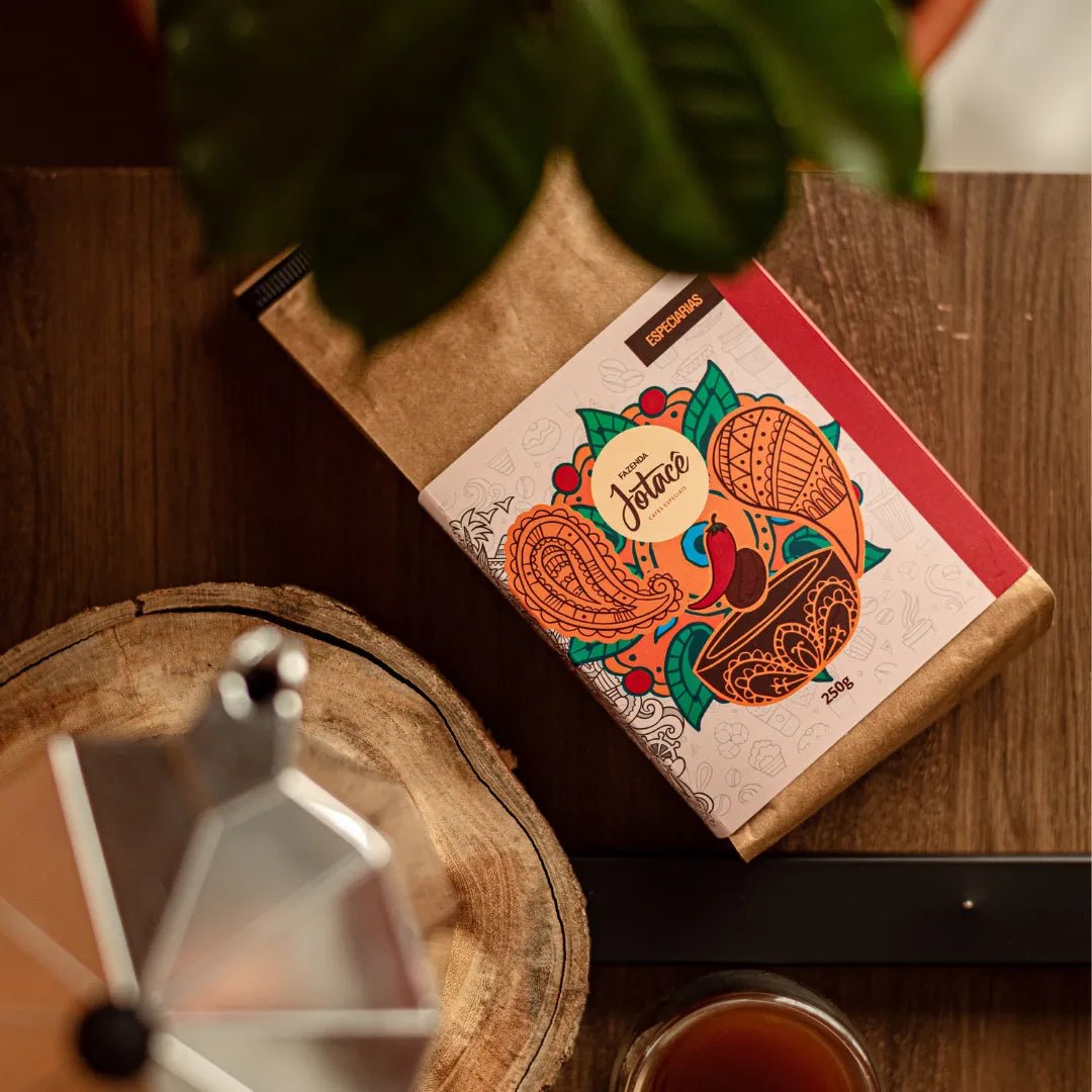 Pacote do Café Especiarias deitado em uma mesa de madeira e ao lado uma cafeteira Italiana desfocada