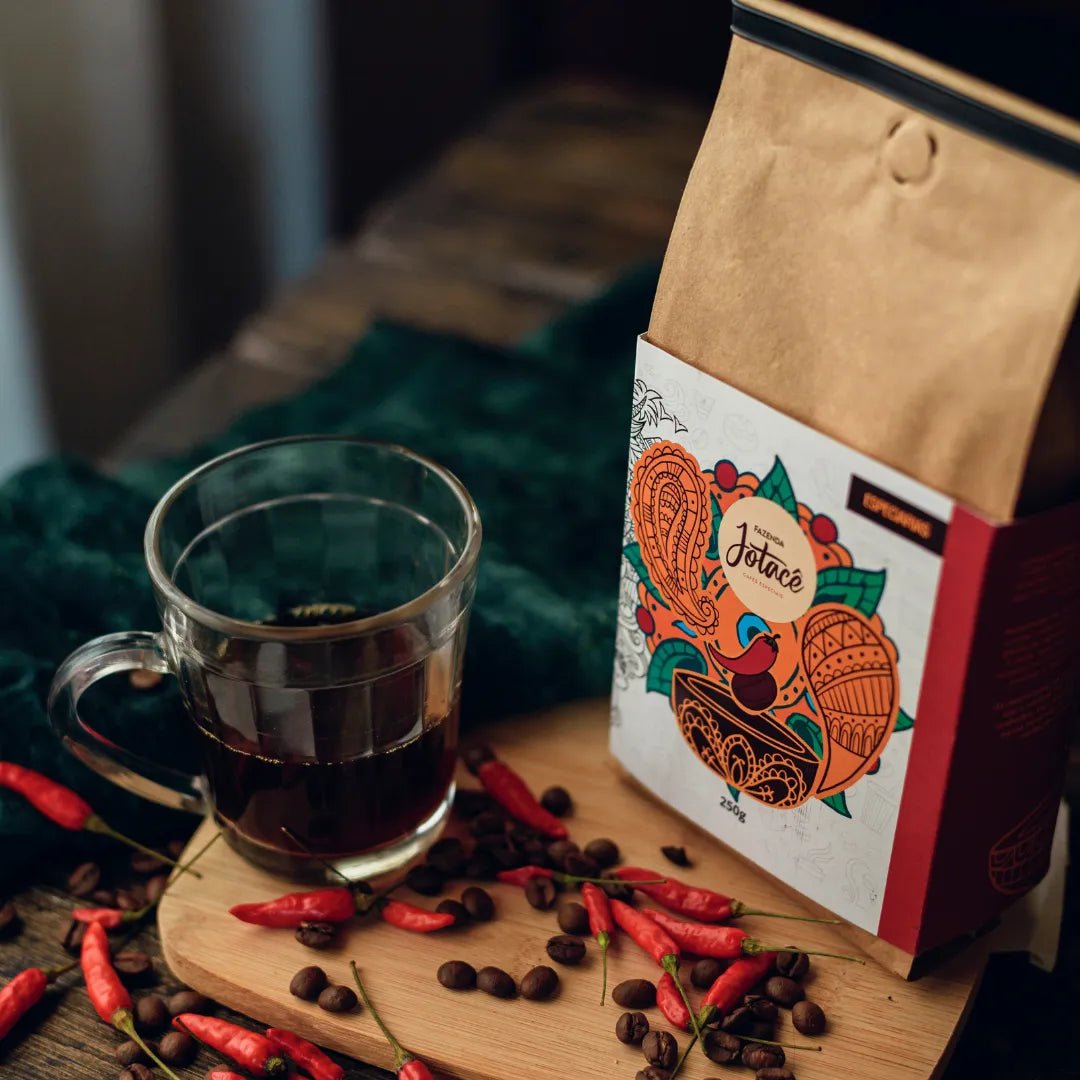 Pacote do café Especiarias ao lado de uma xicara de vidro com café e pimentas e grãos ao redor.