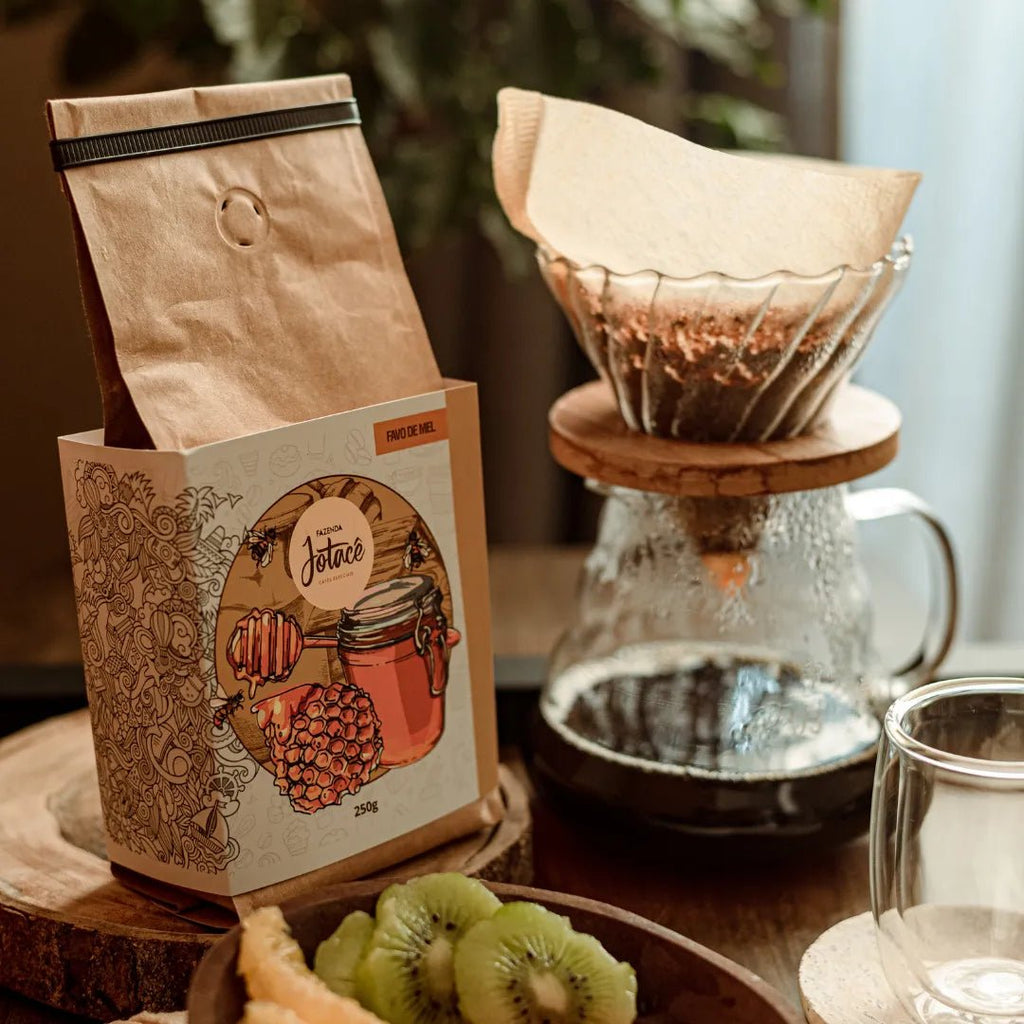 Pacote do café Favo de Mel sobre pedaço de madeira rústica e jarra de café e kiwis cortados ao lado