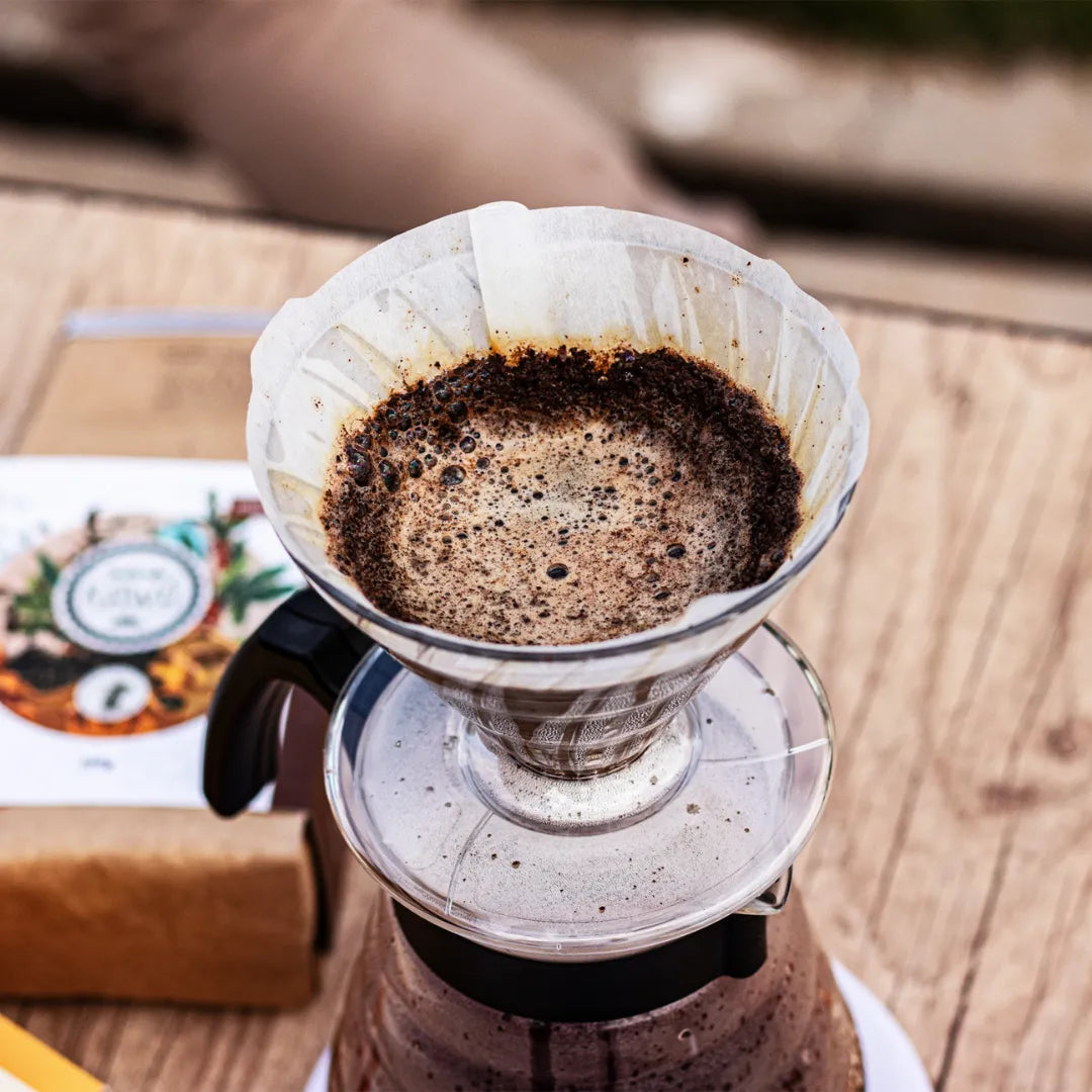 Café soltando bolhas durante o preparo sobre uma mesa rústica de madeira e ao lado um café Kawá Caramelo