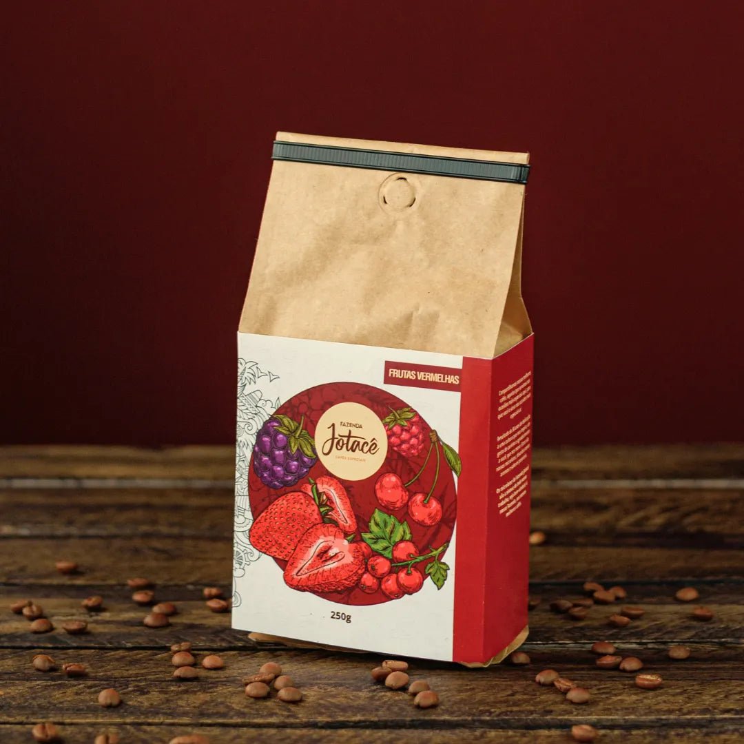 Pacote de café Frutas Vermelhas da Fazenda Jotacê sobre mesa rústica com grãos de café torrado espalhados.