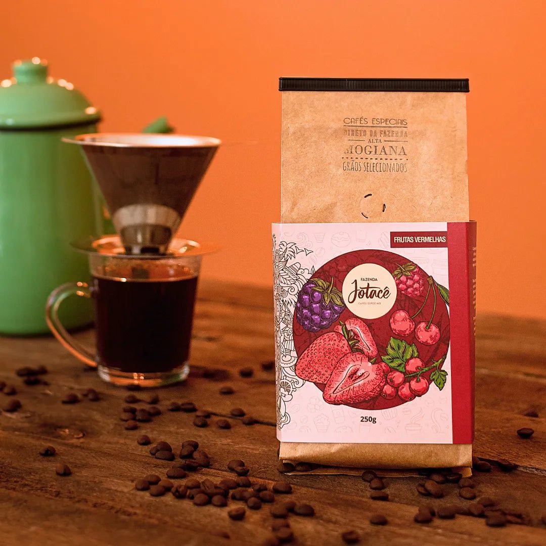 Café Frutas Vermelhas da Fazenda Jotace ao lado de xícara e bule verde ao fundo.