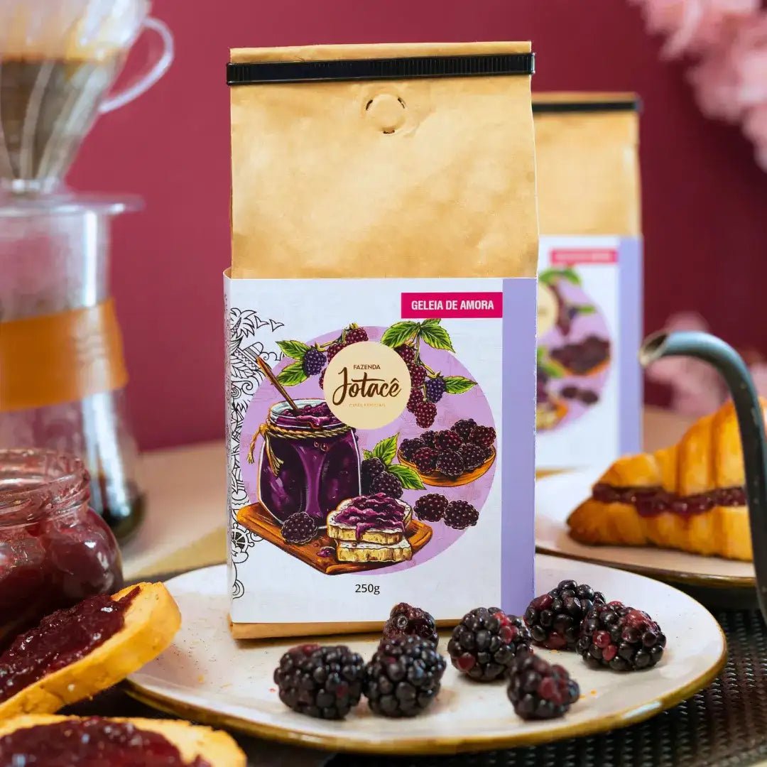 Detalhe do Café Especial Geleia de Amora da Fazenda Jotacê em embalagem de 250g, com ilustração de amoras e mel, acompanhado de frutas frescas e um café coado para uma experiência sensorial completa.