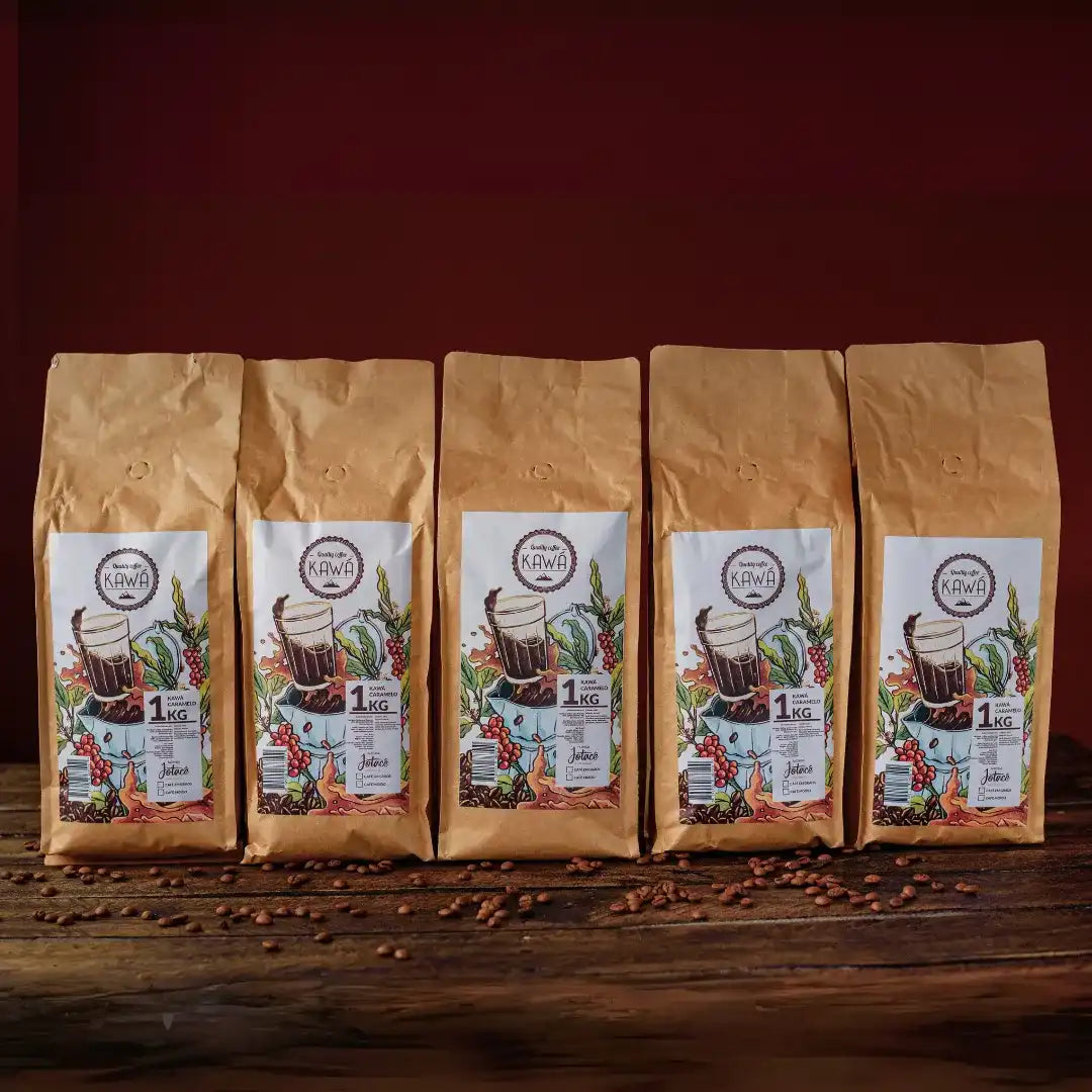 5 pacotes de 1 Kg em pé do produto Kawá Caramelo dispostos lado a lado sobre mesa de madeira com grãos soltos