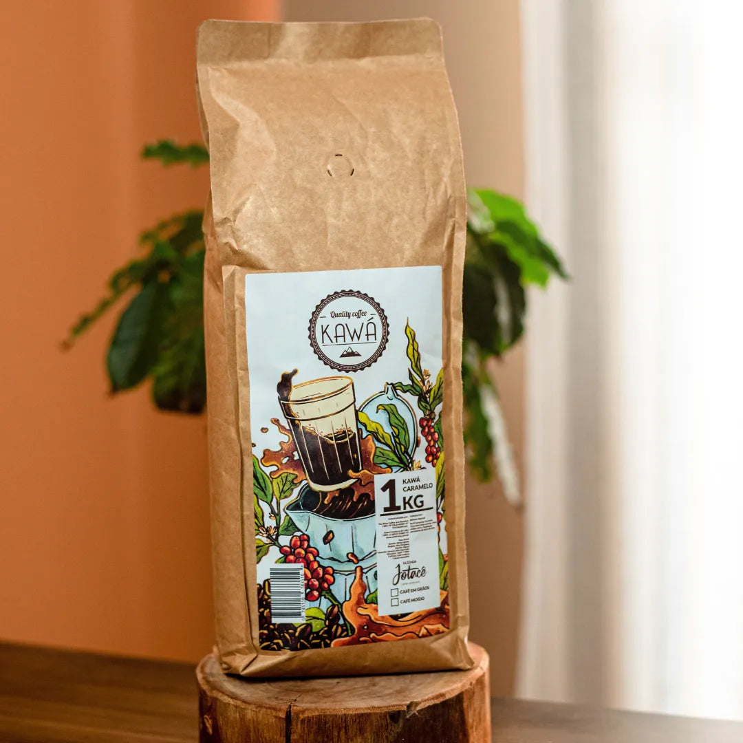 Vista frontal de um pacote de 1 Kg de Café Kawa Caramelo da Fazenda Jotacê e uma planta sobre mesa e aparador de madeira
