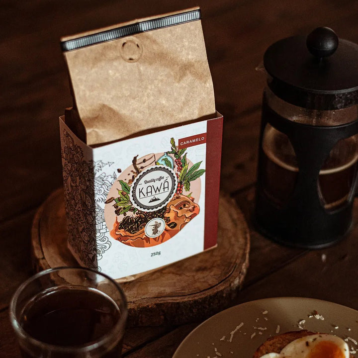 Vista isométrica do Pacote de 250g do café Kawá Caramelo da Fazenda Jotacê, ao lado de uma xícara e prensa francesa