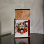 Pacote de 250g do Café naturalmente doce Kawá Caramelo da Fazenda Jotacê, sobre a quina de uma mesa com fundo desfocado