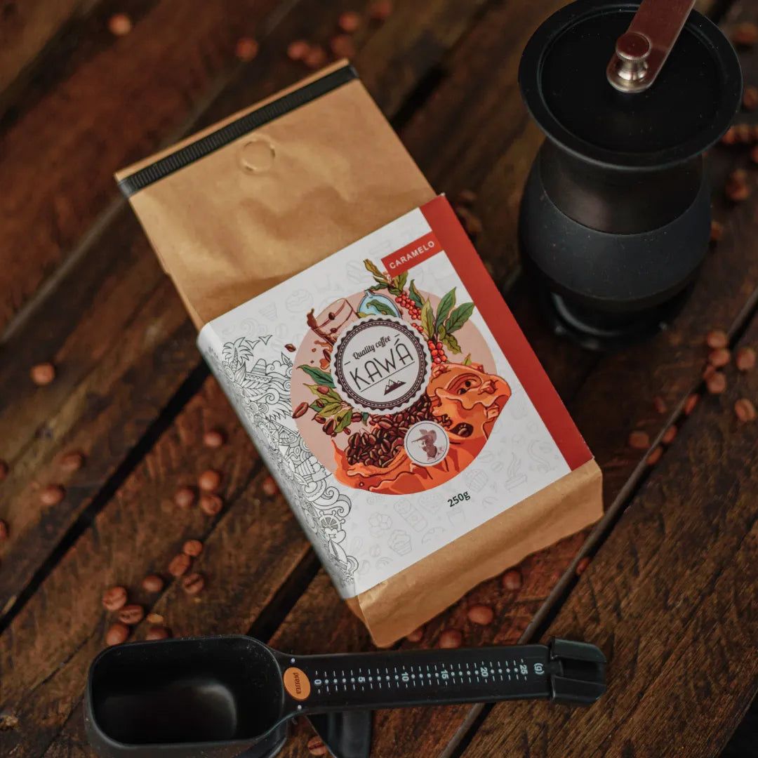 Kit de preparo de café com pacote de Café Kawá, moedor manual e balança, sobre mesa de madeira.