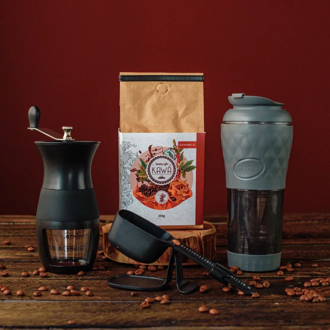 Equipamento de café com moedor manual, pacote de café Kawá, balança e cafeteira portátil Pressca, em uma mesa de madeira.
