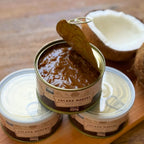 Lata de Cocada Morena 400g recém-aberta, mostrando a textura espessa da cocada, com um coco partido ao fundo em um cenário rústico.