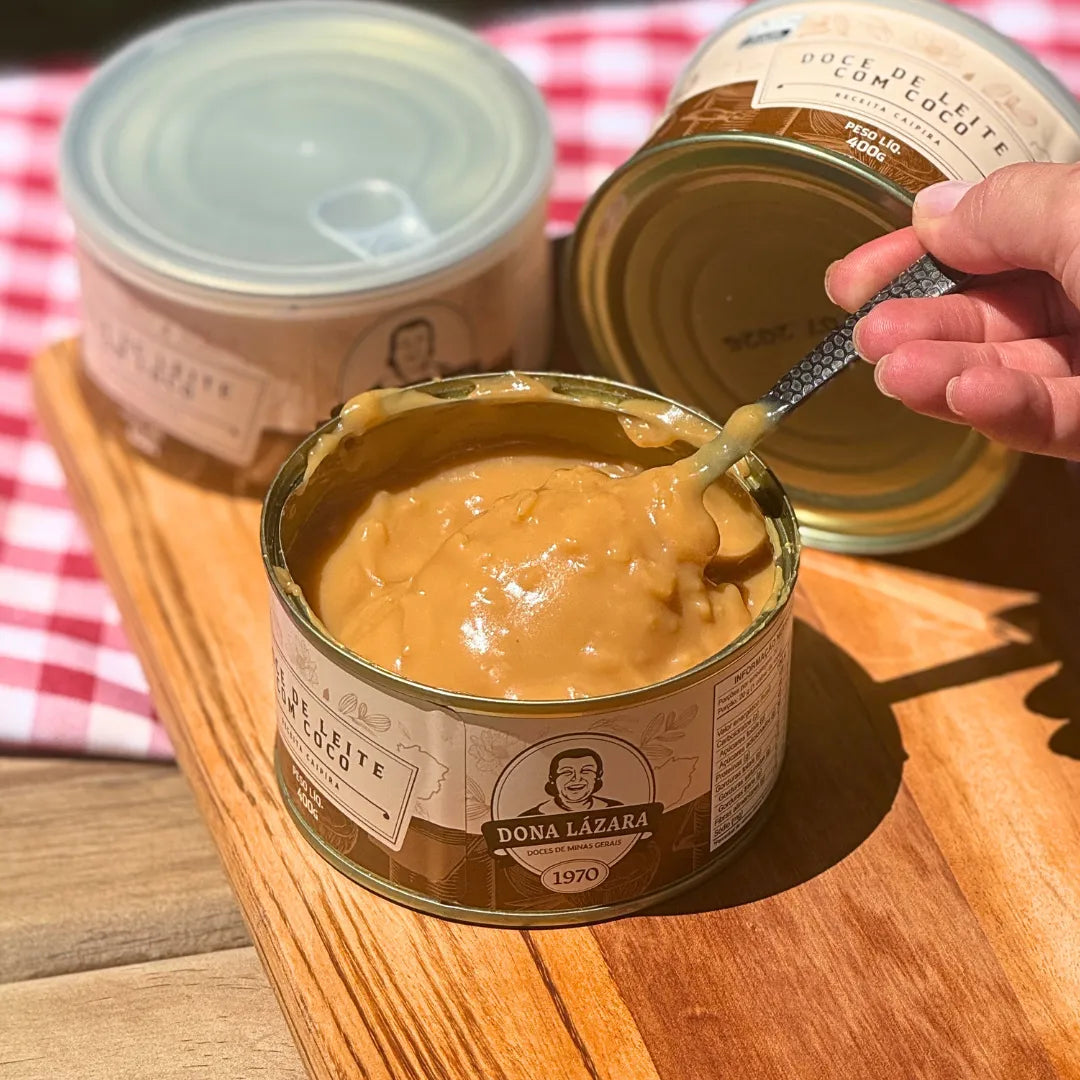 Doce de Leite com Coco 400g sendo servido com colher, destacando a cremosidade e os pedaços de coco.