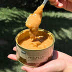 Lata aberta de Doce de Leite com Coco 400g, mostrando a textura cremosa do doce com colher apoiada na borda.