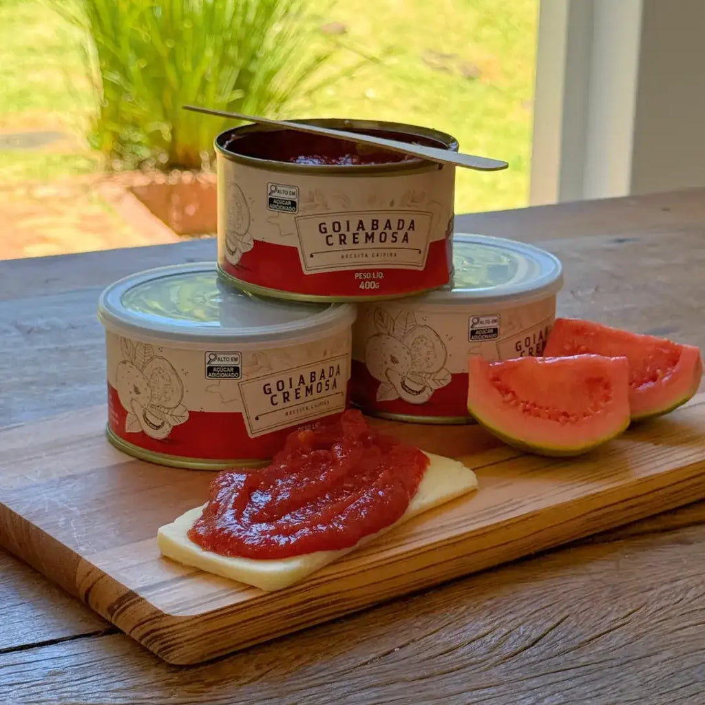 Lata aberta de goiabada cremosa com colher e fatia de queijo com doce de goiaba cremoso ao lado.