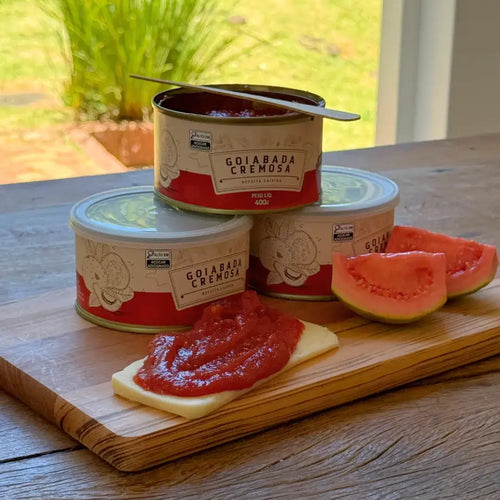 Lata aberta de goiabada cremosa com colher e fatia de queijo com doce de goiaba cremoso ao lado.