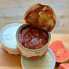 Três latas de goiabada cremosa e fatias de goiaba fresca com queijo minas sobre tábua de madeira.