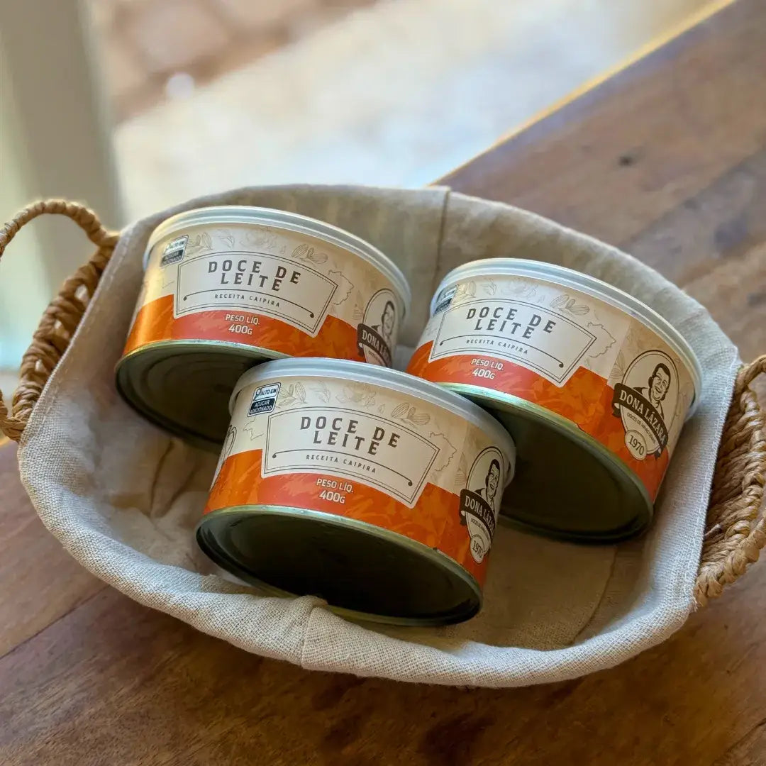 Latas de Doce de Leite Receita Caipira 400g organizadas em uma cesta de tecido, mostrando a embalagem artesanal e rótulo tradicional.