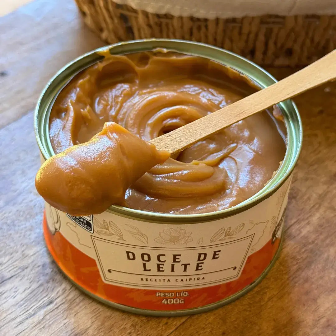 Lata de Doce de Leite Receita Caipira 400g aberta, com textura cremosa sendo servida com uma espátula de madeira.