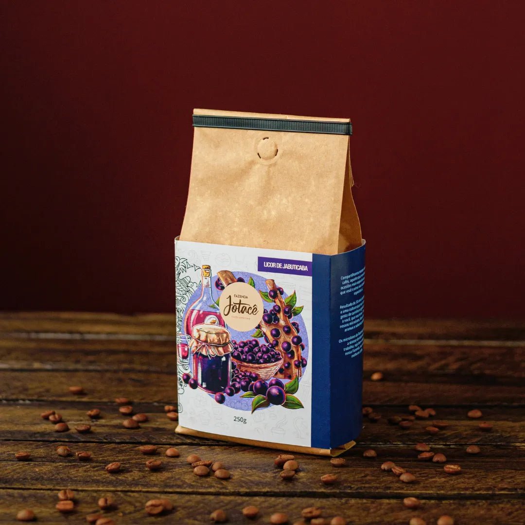 Pacote de café Licor de Jabuticaba sobre uma mesa de madeira e diversos grãos de café espalhados