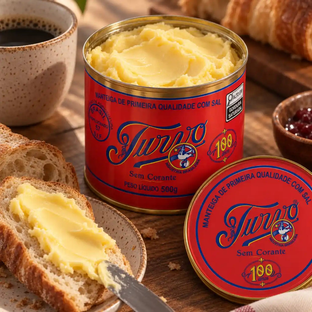 Lata aberta de Manteiga Turvo com sal com a manteiga cremosa em destaque, tampa vermelha ao lado, fatia de pão passada com manteiga, xícara de café e tigela de geleia sobre mesa rústica.