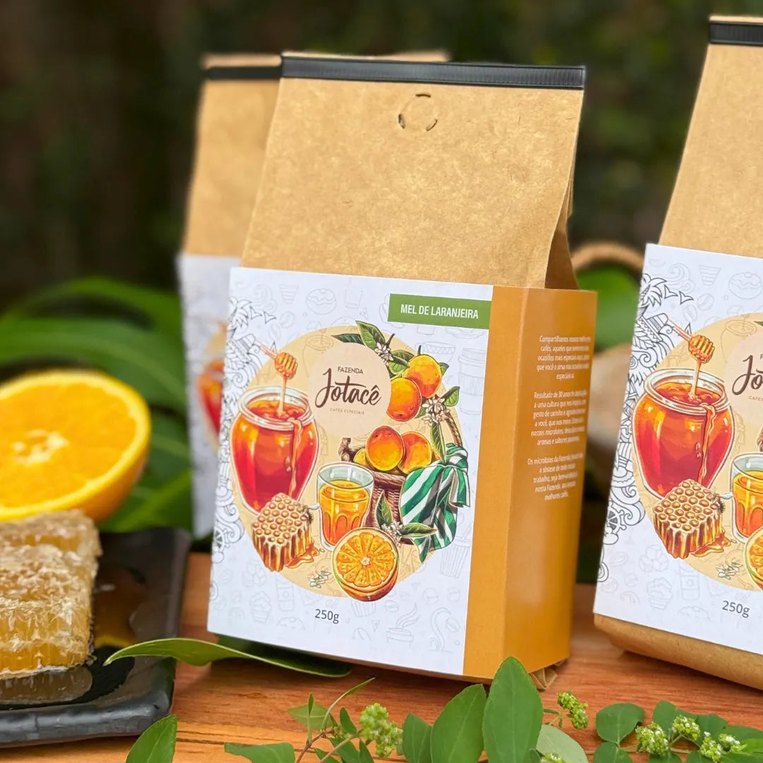 Café especial Mel de Laranjeira da Fazenda Jotacê em ambiente natural, acompanhado de laranjas frescas, folhas verdes e favo de mel, destacando suas notas cítricas e doçura natural.