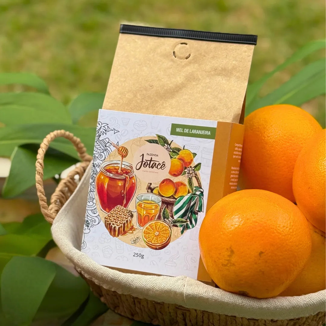 Embalagem do café Mel de Laranjeira da Fazenda Jotacê em cesta rústica com laranjas maduras, remetendo à doçura natural e às notas cítricas do microlote.