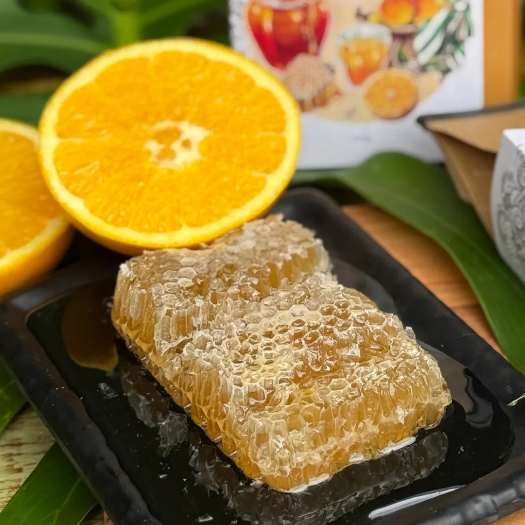 Detalhe do café Mel de Laranjeira da Fazenda Jotacê com favo de mel e laranja fresca em primeiro plano, representando sua doçura natural e perfil sensorial cítrico.