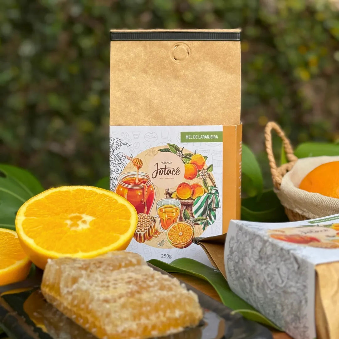Café especial Mel de Laranjeira da Fazenda Jotacê em cenário natural com laranjas, folhas verdes e favo de mel, evocando um café doce, cítrico e artesanal.