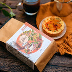 Café Microlote Moca ao lado de um quiche e uma xícara de café sobre mesa rústica de madeira